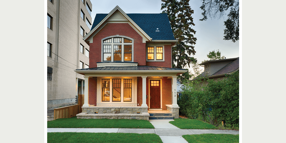 A red brick home with Sterling double hung windows overlooks the street. Columns frame the front porch and the Craftsman-style wooden door. 